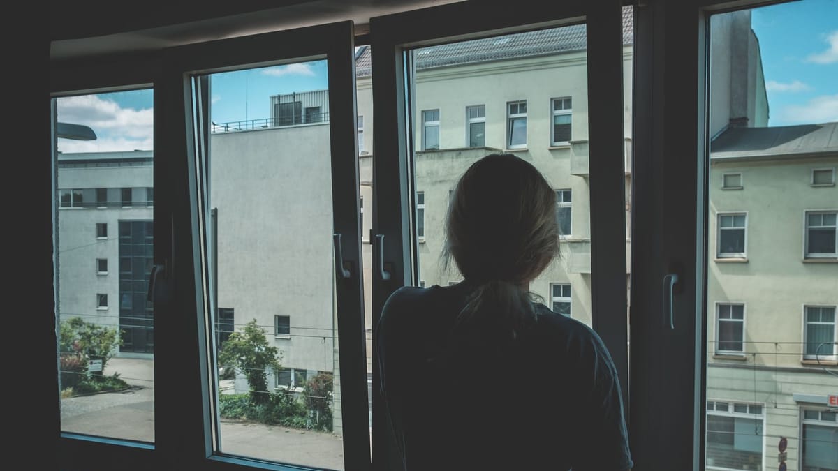 Young woman seen from behind looking out a window