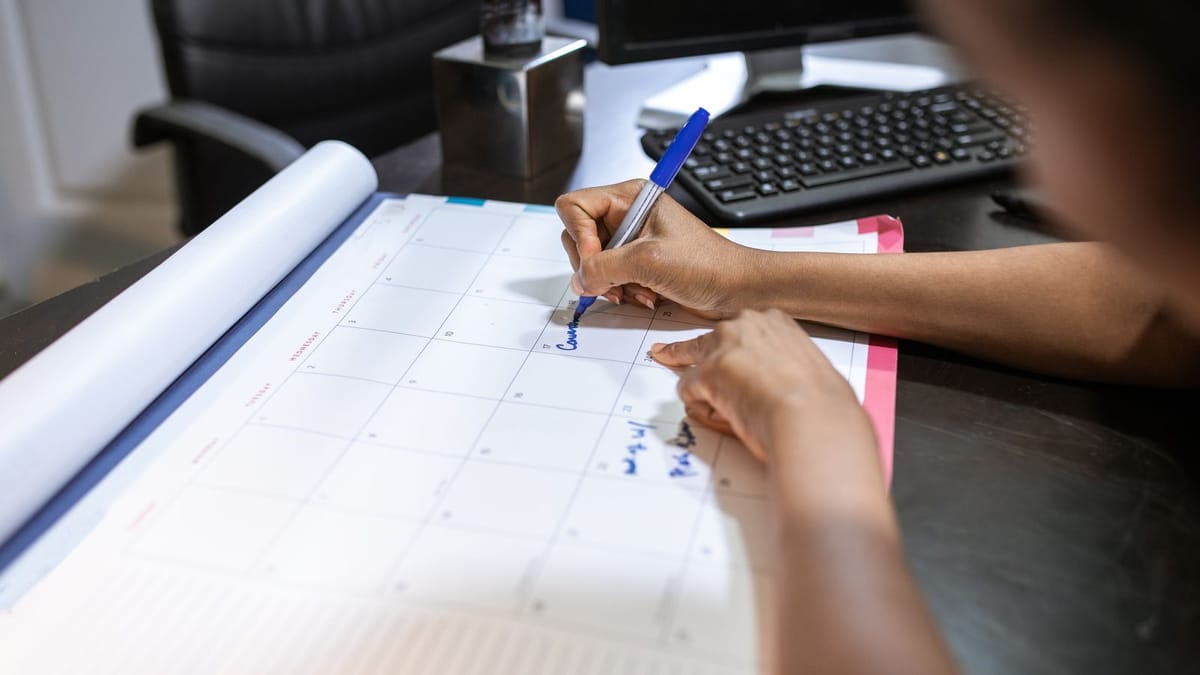 Femme notant des dates sur un calendrier mensuel de bureau