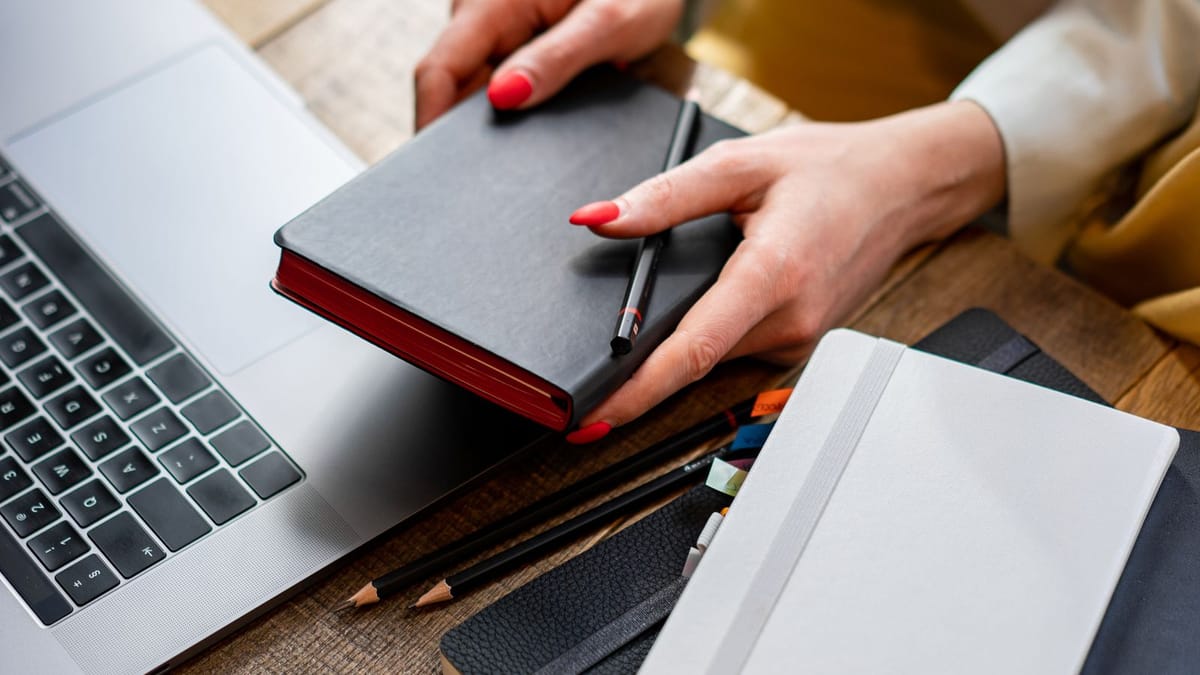 Mains féminines aux ongles rouges rangeant des carnets près d'un ordinateur
